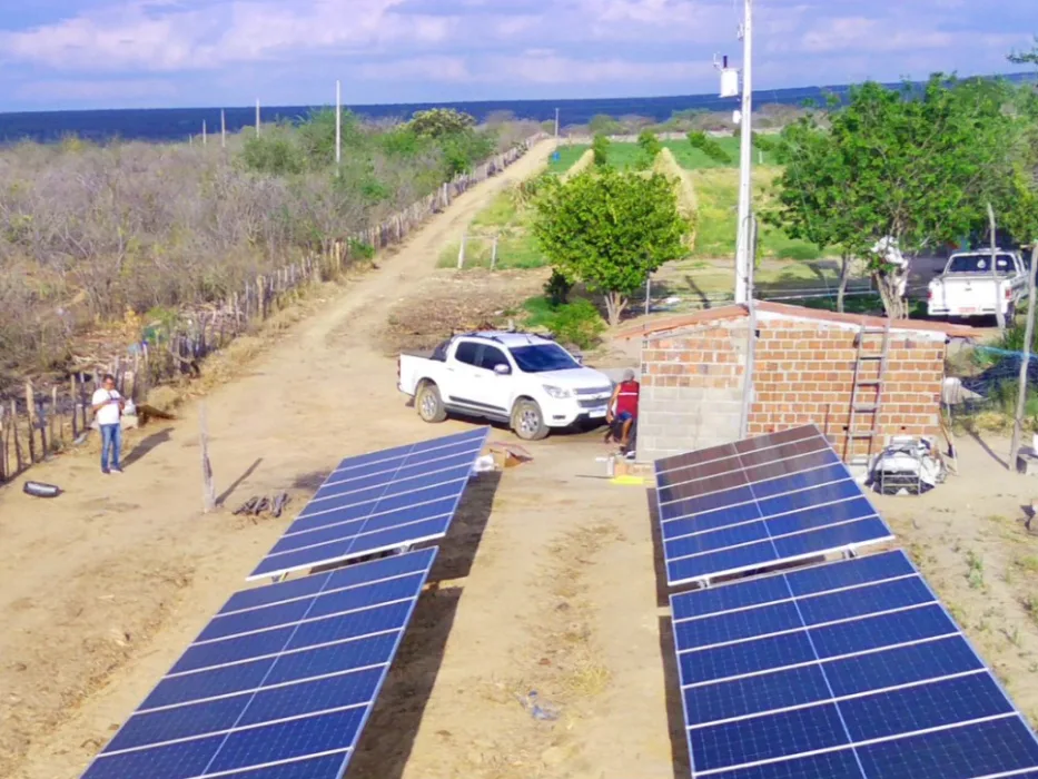 Duas fileiras de módulos fotovoltaicos em estrutura de solo ao lado de casa de tijolo, na zona rural de Ibimirim-PE